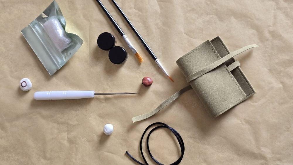The KEGO kit laid out: clay, two pots of paint, varnish, brush, bead tool and the bracelet cord.